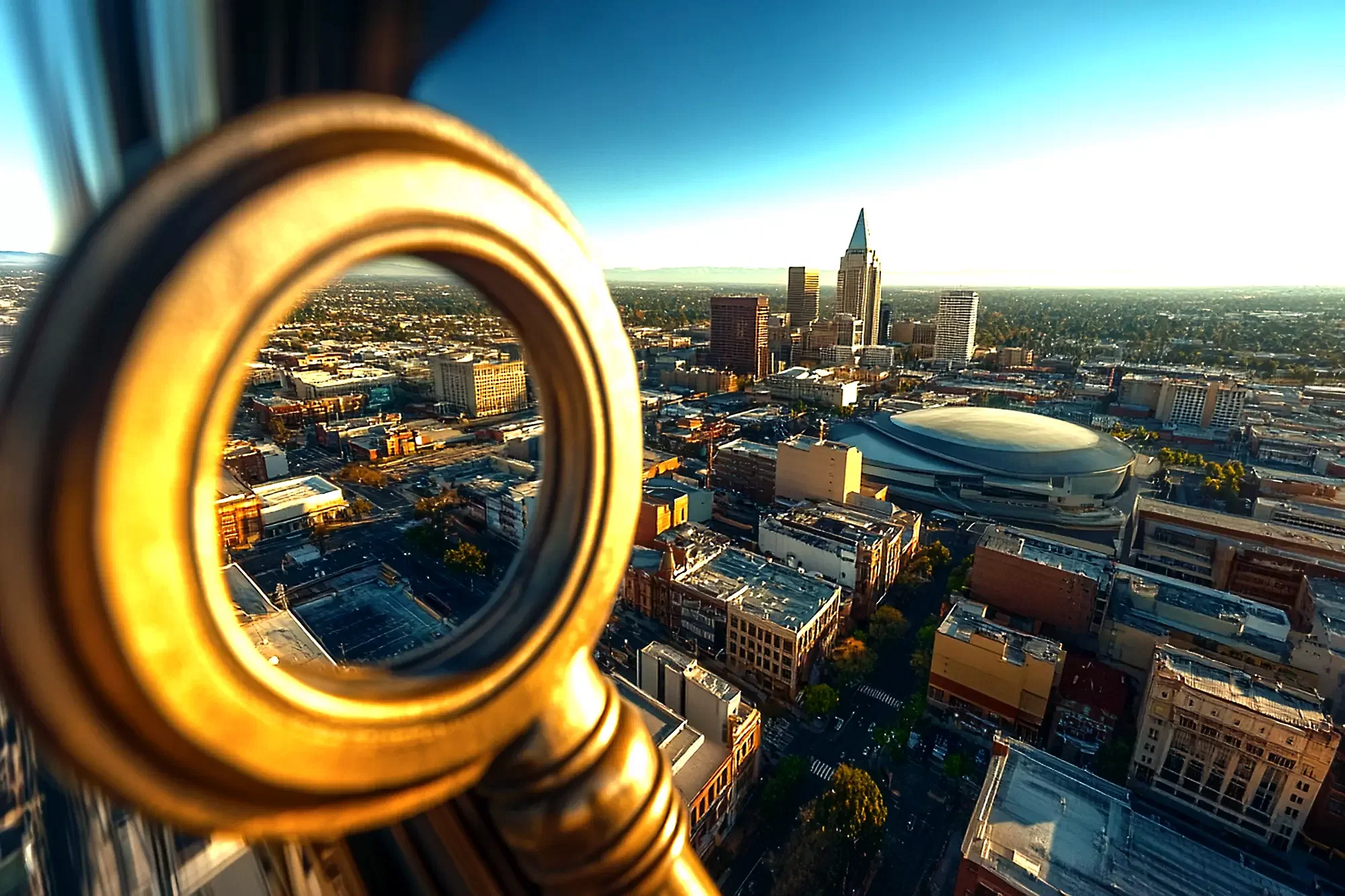 Aerial view of Stockton's cityscape with a large key in the foreground. Prominent buildings and a circular arena grace the skyline, representing SLPM Association Management, all under a clear blue sky.