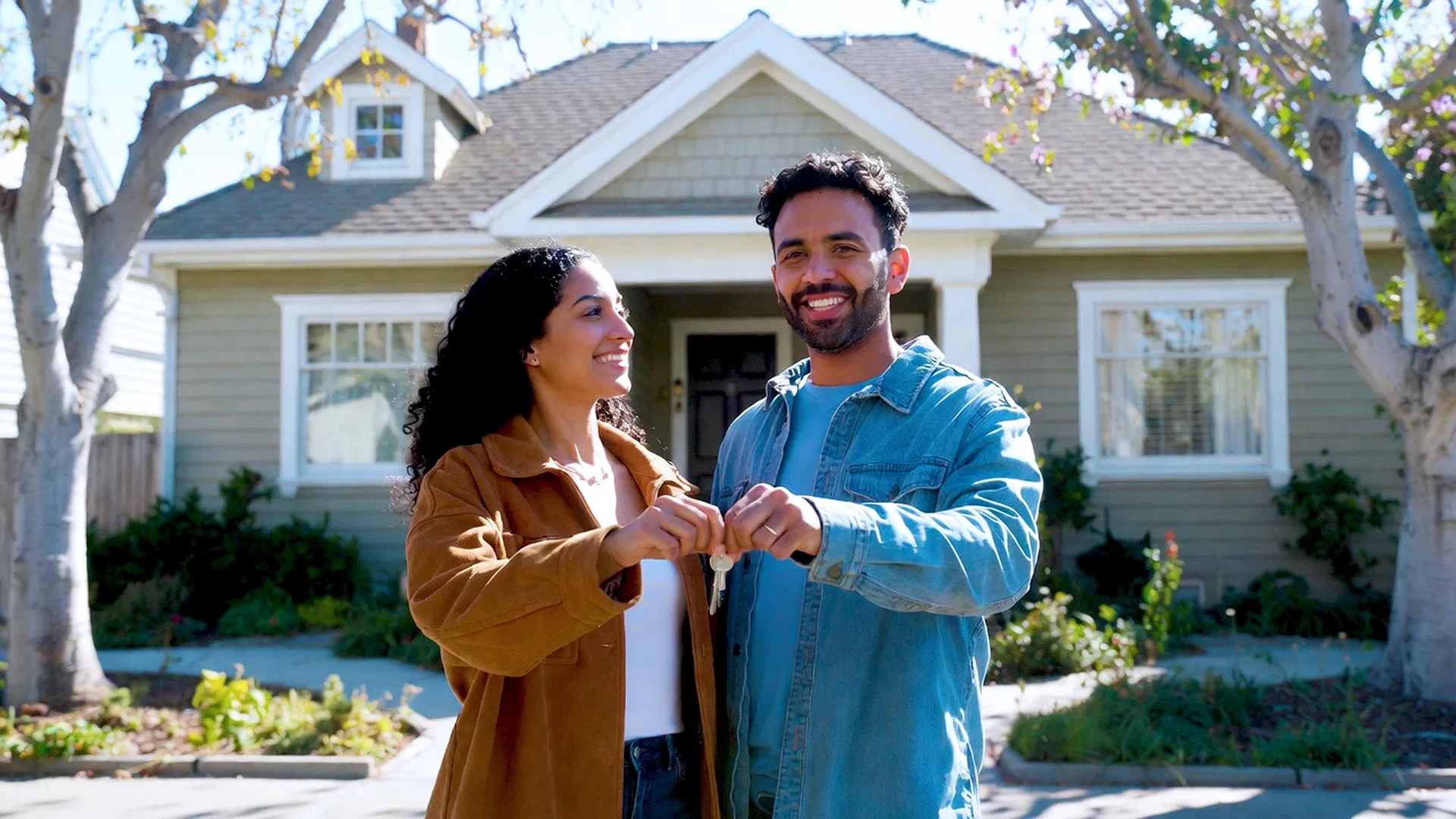 A smiling man and woman stand in front of their new house, giving each other a fist bump—celebrating as first-time homebuyers with the California Dream For All program in 2026.